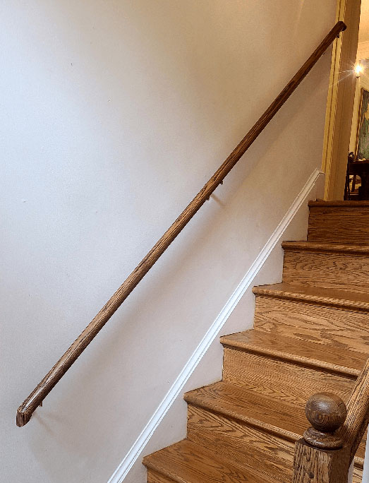 Round wood railing installation in Silverspring, MD  on a white wall  and stained to match  the staircases and banister railing on the opposite side