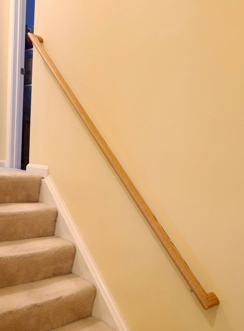 Oval wood railings with returns installed on the right side of a wall with carpeted staircase in Potomac, MD