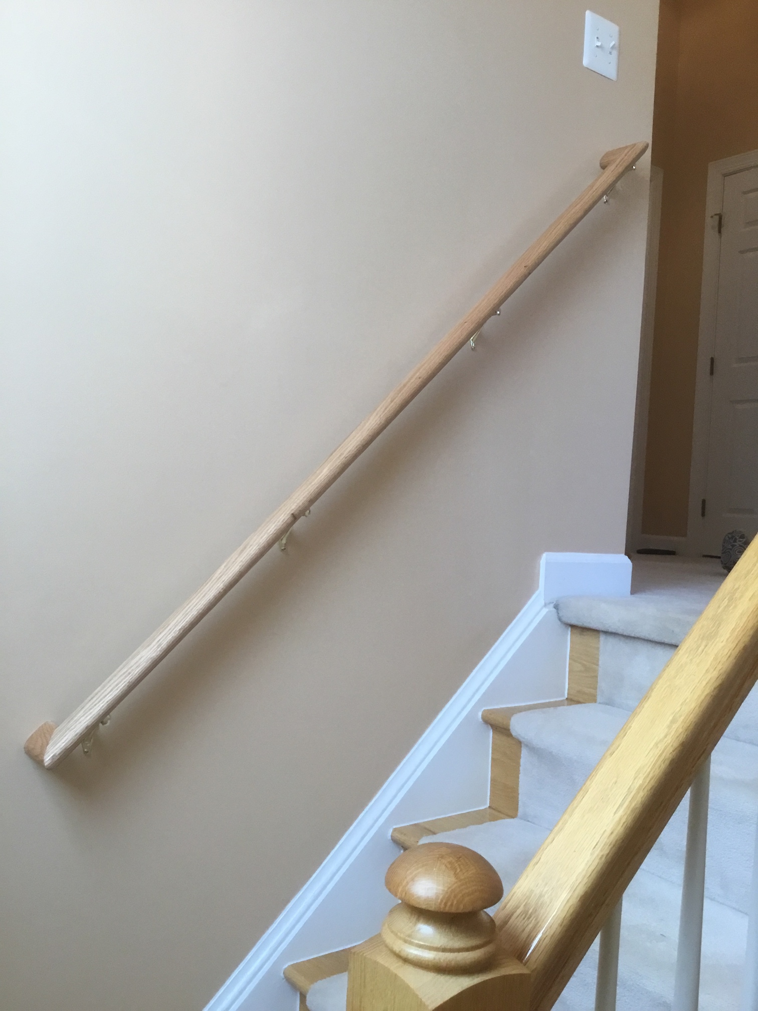 Wood railing with returns installed on the left side of white carpeted staircase in Kensington, MD